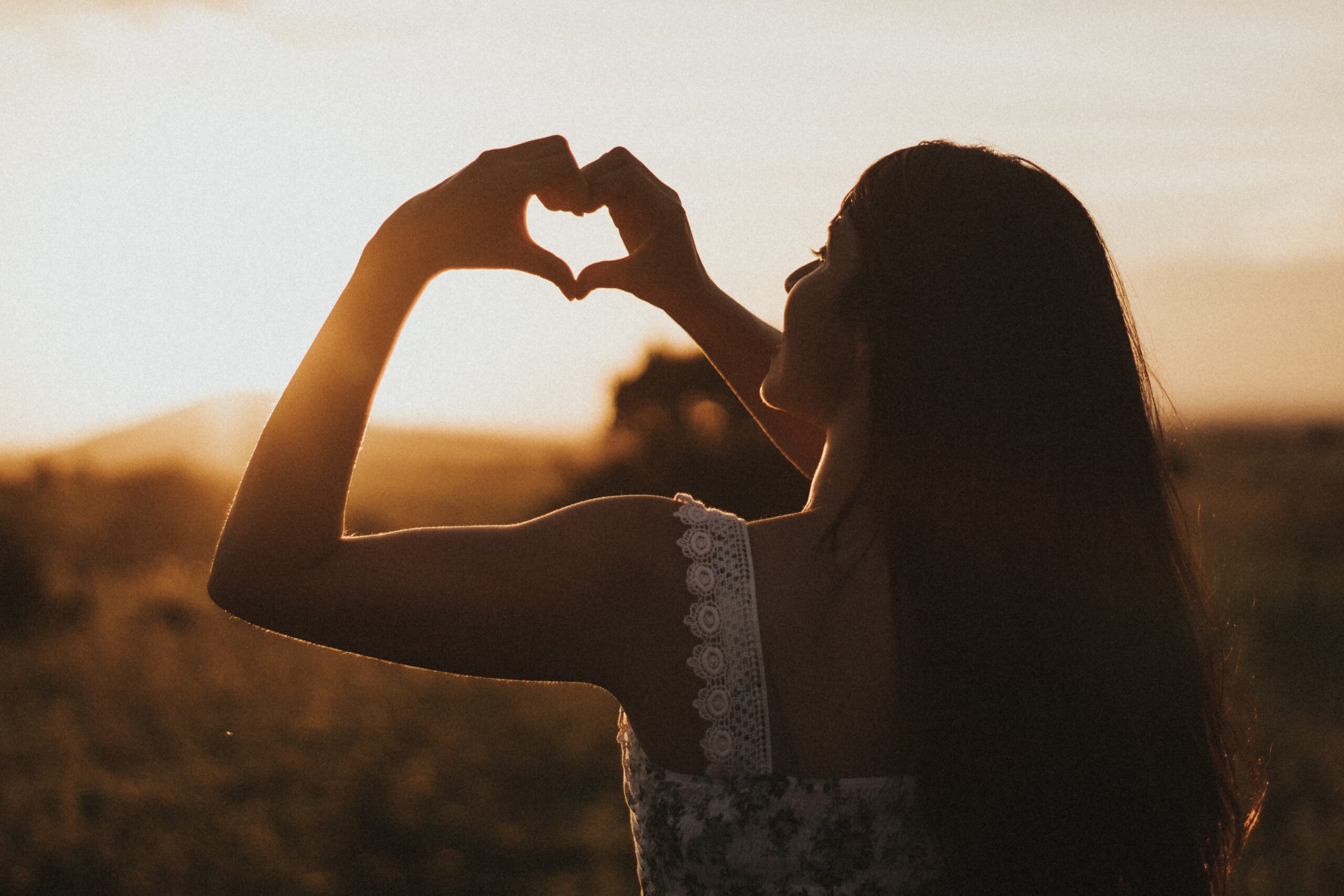 A Woman Making Heart From Her Hand Infront of Sunset.