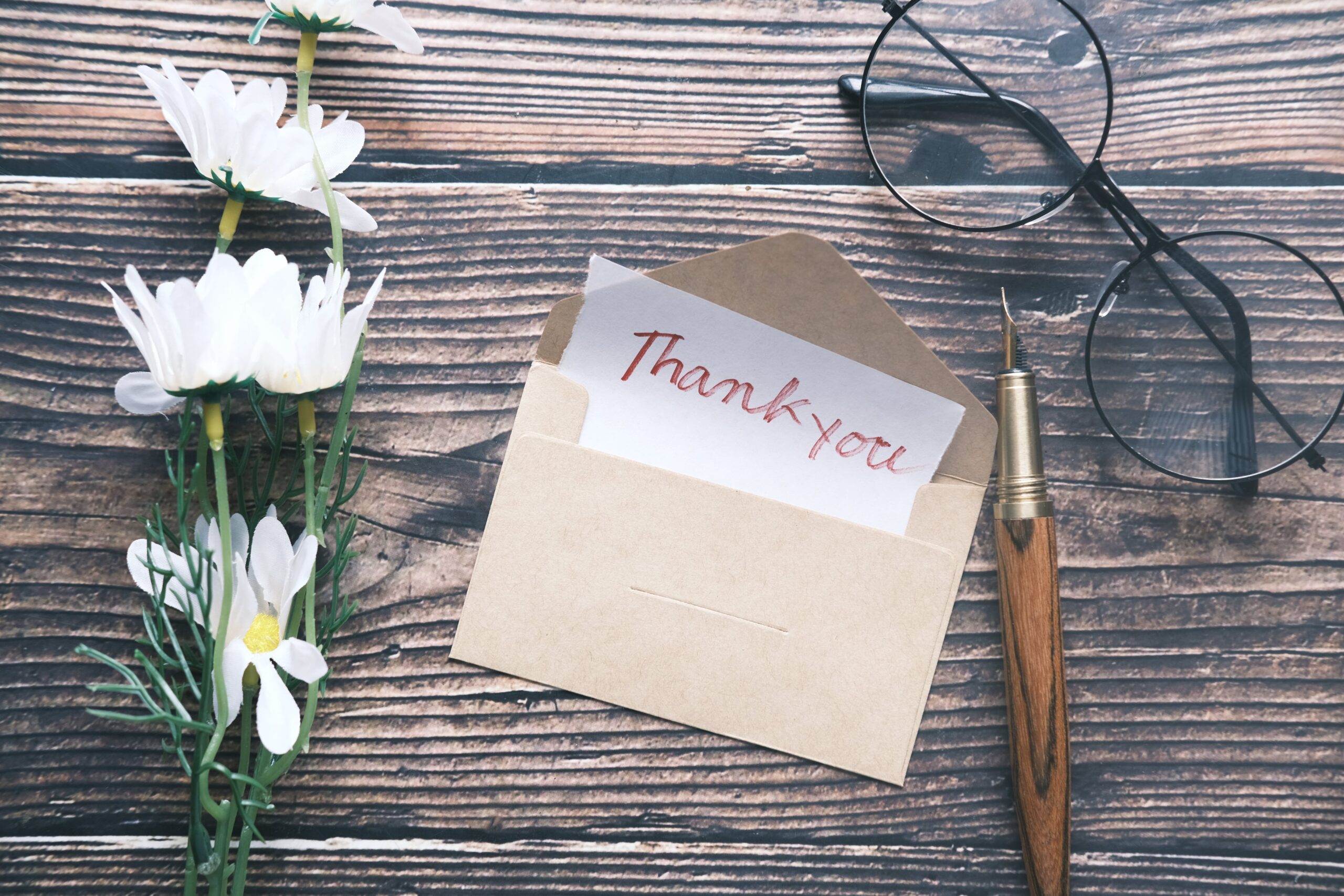 Thank You Note Written on Paper With a Flower and Glasses Positioned Nearby