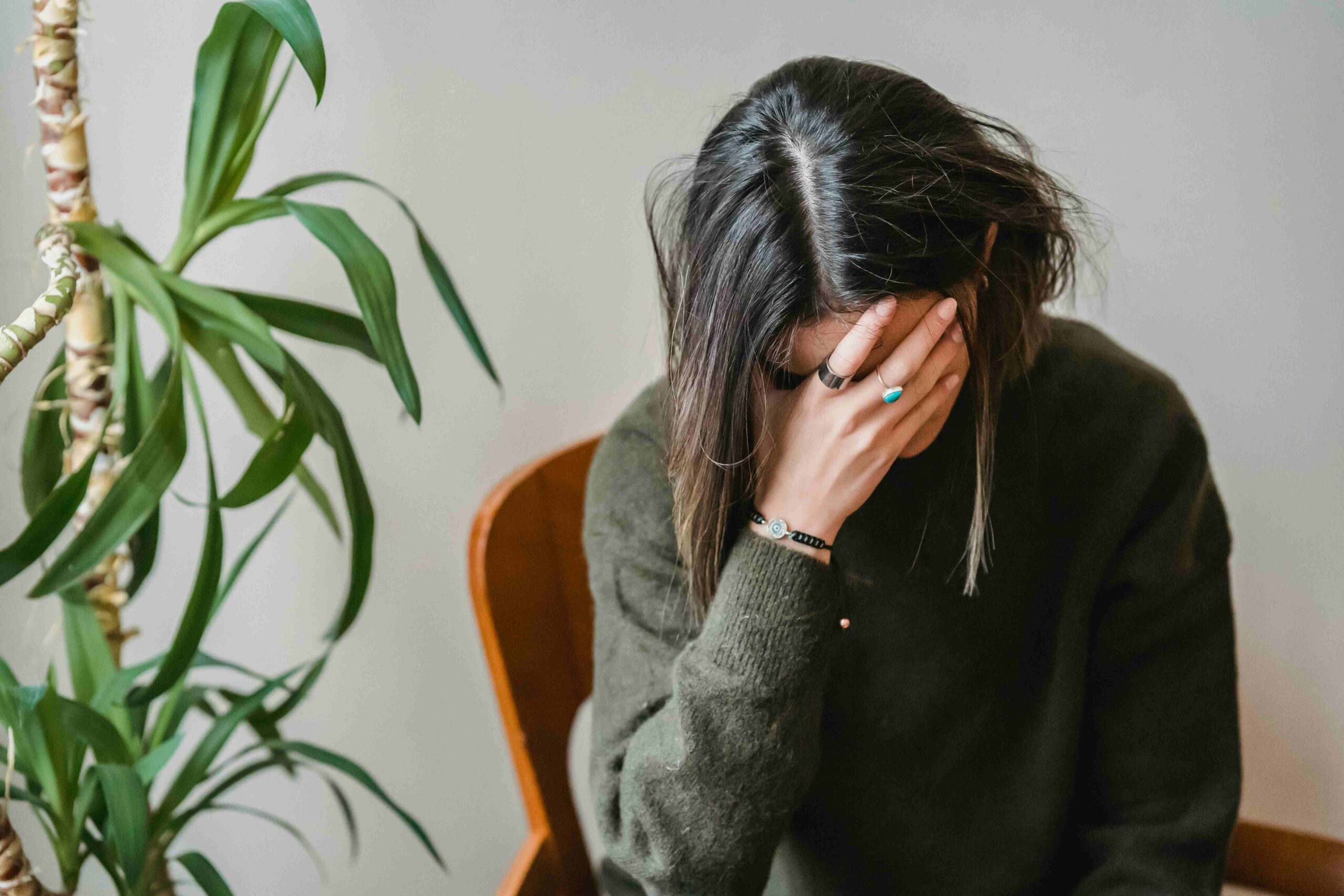 A woman sits on a chair, her head resting in her hands, conveying a sense of distress or deep contemplation.