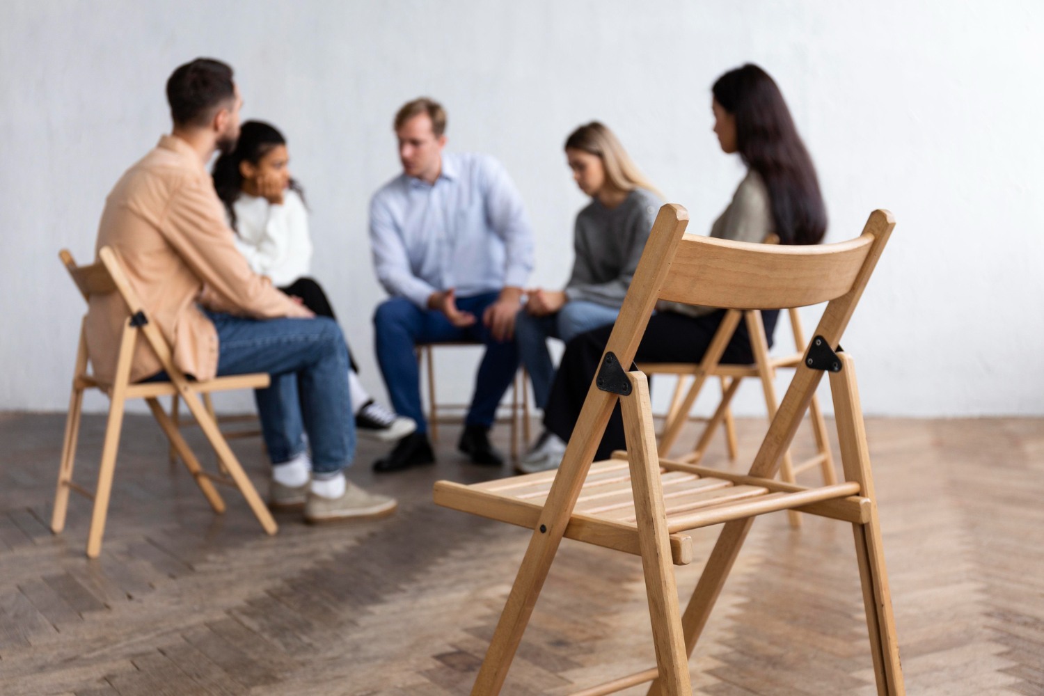 A diverse group of individuals engaged in conversation while seated around a table in a well-lit room.