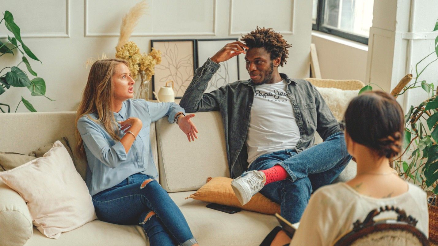 A couple talk to each other on a therapist’s couch during a session.